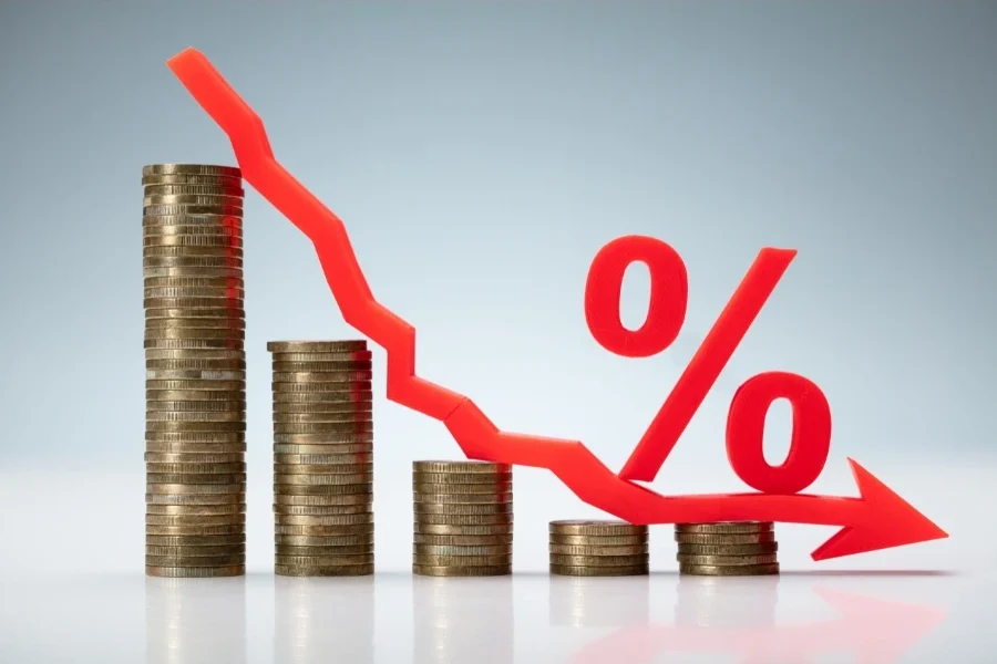 Grafico con monete e freccia rossa discendente che rappresenta il calo dei tassi d’interesse ma aumento delle spese bancarie